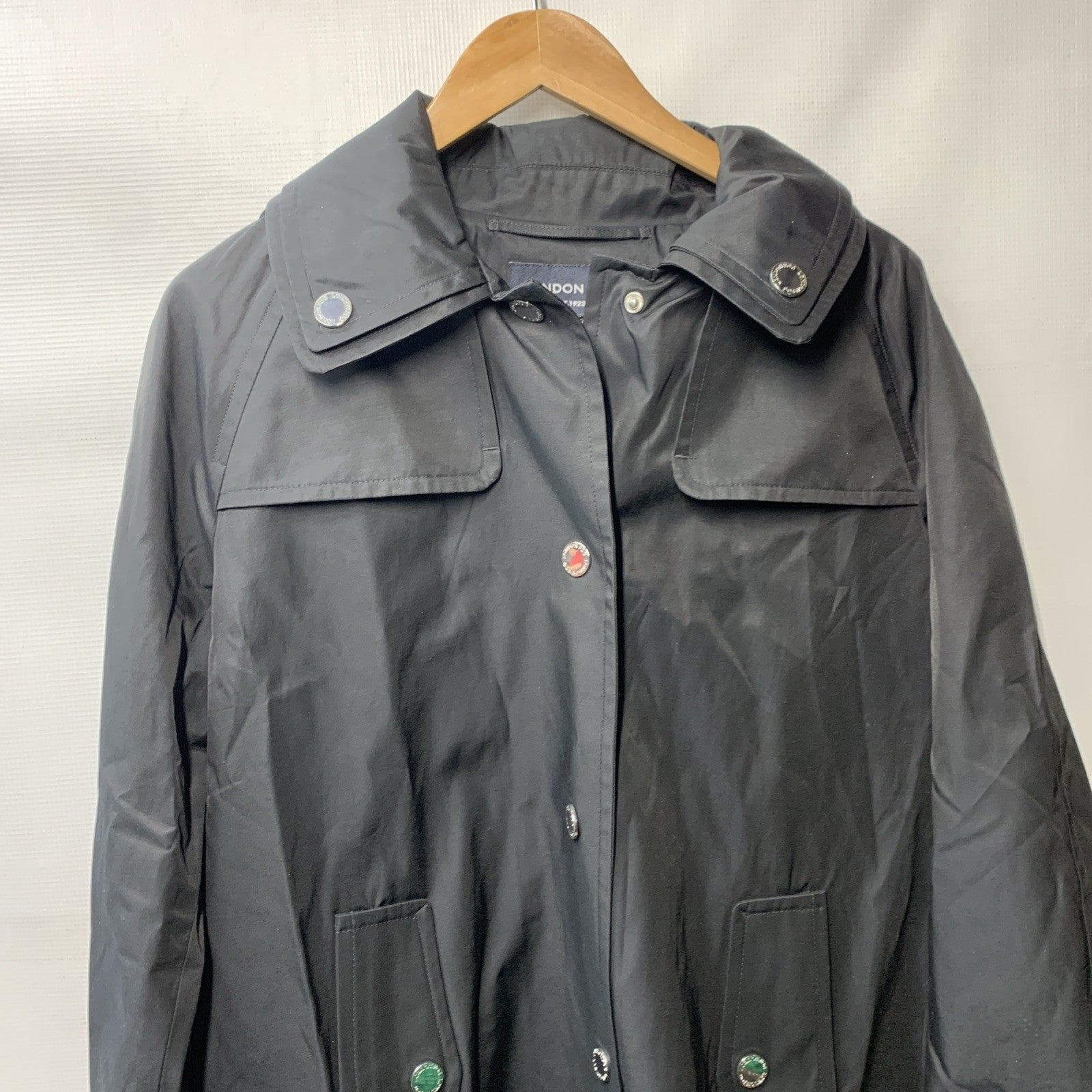 Black London Fog women's trench coat with hood, long sleeves, and pockets, displayed on a hanger.
